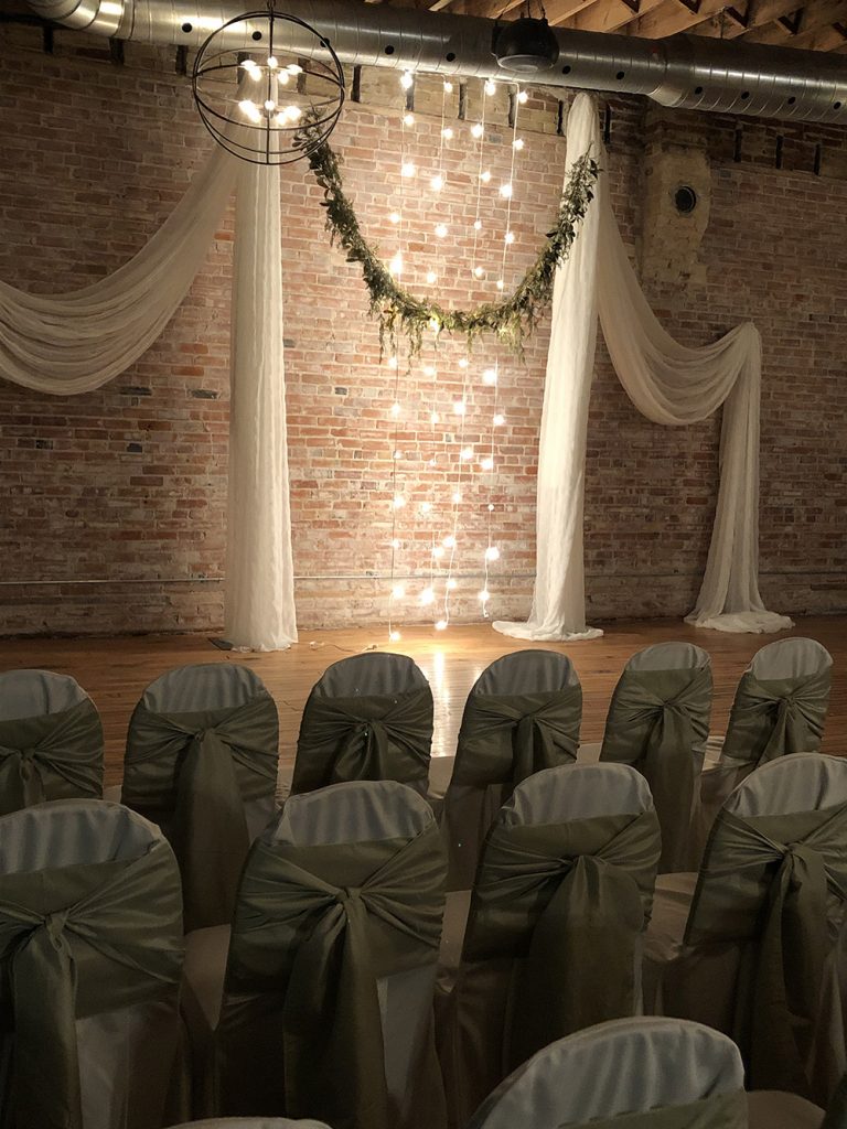 brick wall wedding ceremony decor with pillars, lights and greenery now & always