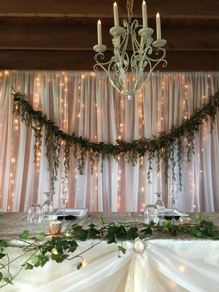 head table with white backdrop with lights and greenery