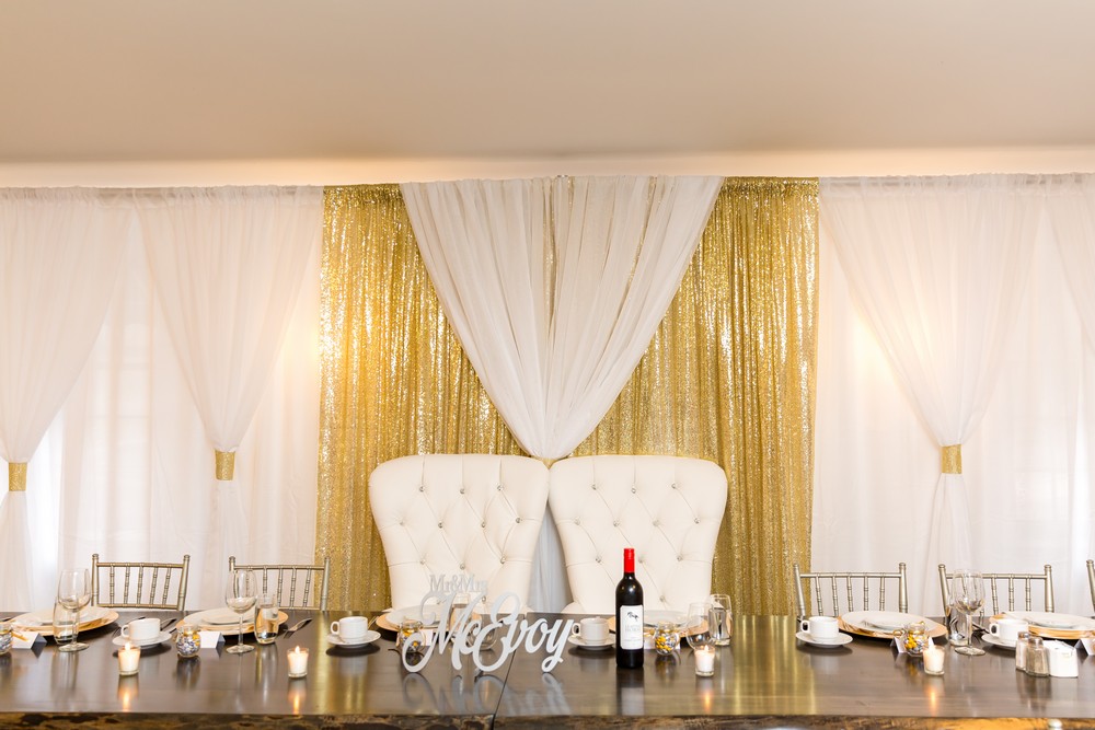 gold and white backdrop behind a head table with king and queen chairs