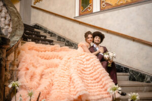 French luxury nspired wedding, bride and groom sitting together on a grand flight of stairs, Bride in a peach ruffled wedding dress