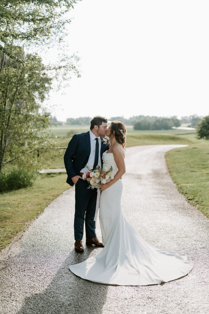 Rebel Creek Golf Club, Colour Elegance, bride and groom kissing on a dirt path with a golf course in the background