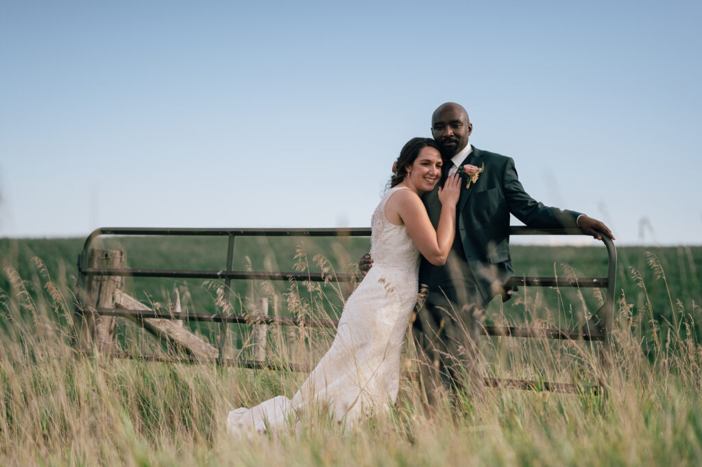 Casual boho wedding, bride and groom hugging looking at the camera, they are leaning on a stone wall